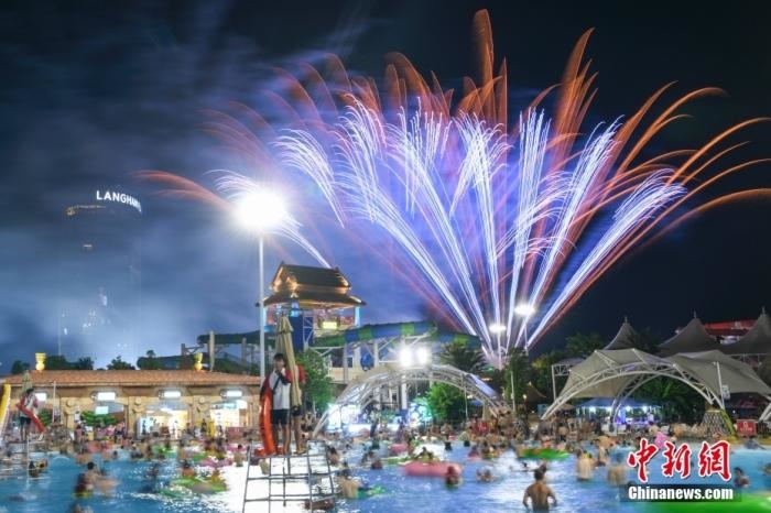 7月20日晚，市民在長沙湘江歡樂城歡樂水寨水池中嬉戲避暑，并欣賞天空燃放的煙火。 <a target='_blank' href='/'>中新社</a>記者 楊華峰 攝